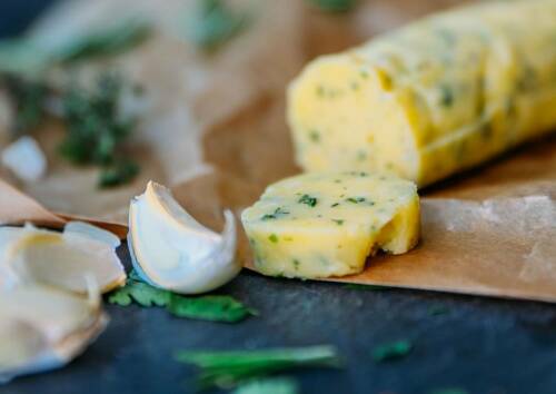 Kräuterbutterrolle auf Backpapier mit Knoblauchzehe