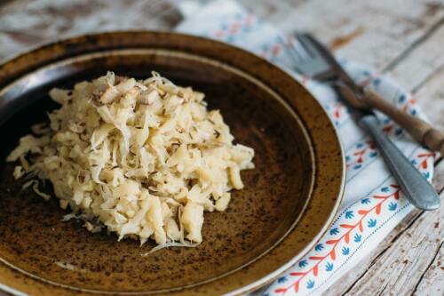 Vegane Krautspatzn auf braunem Teller neben Besteck vor hellem Hintergrund.