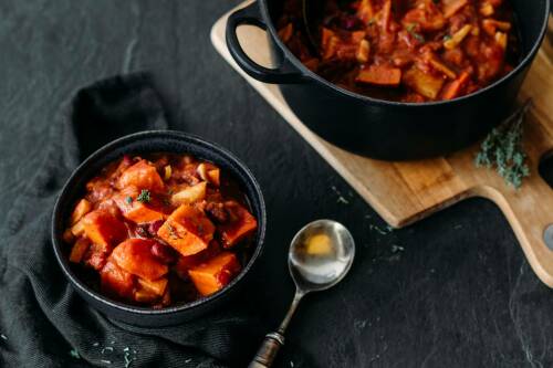 Kürbis Bohnen Eintopf in Schüssel und Topf vor dunklem Hintergrund.