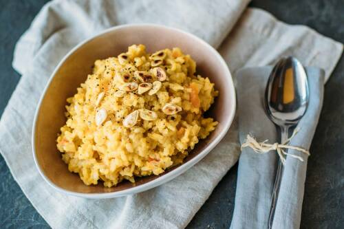 Kürbis-Risotto in weißer Schüssel neben Löffel vor hellem Hintergrund.