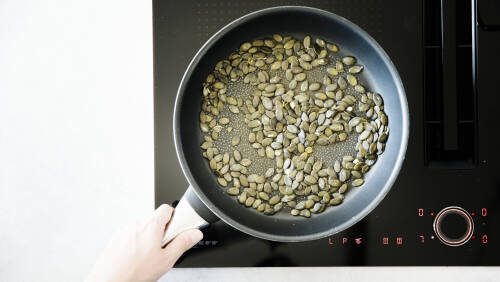 Kürbiskerne rösten in Pfanne auf Herd.