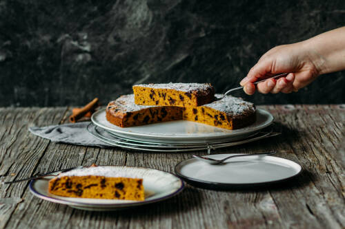 Kürbiskuchen auf Teller mit Hand vor dunklem Hintergrund.