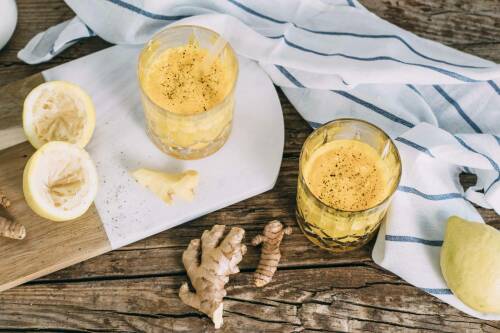 Kurkuma Ingwer Immunbooster in Gläsern neben Ingwer und Zitrone vor dunklem Hintergrund.