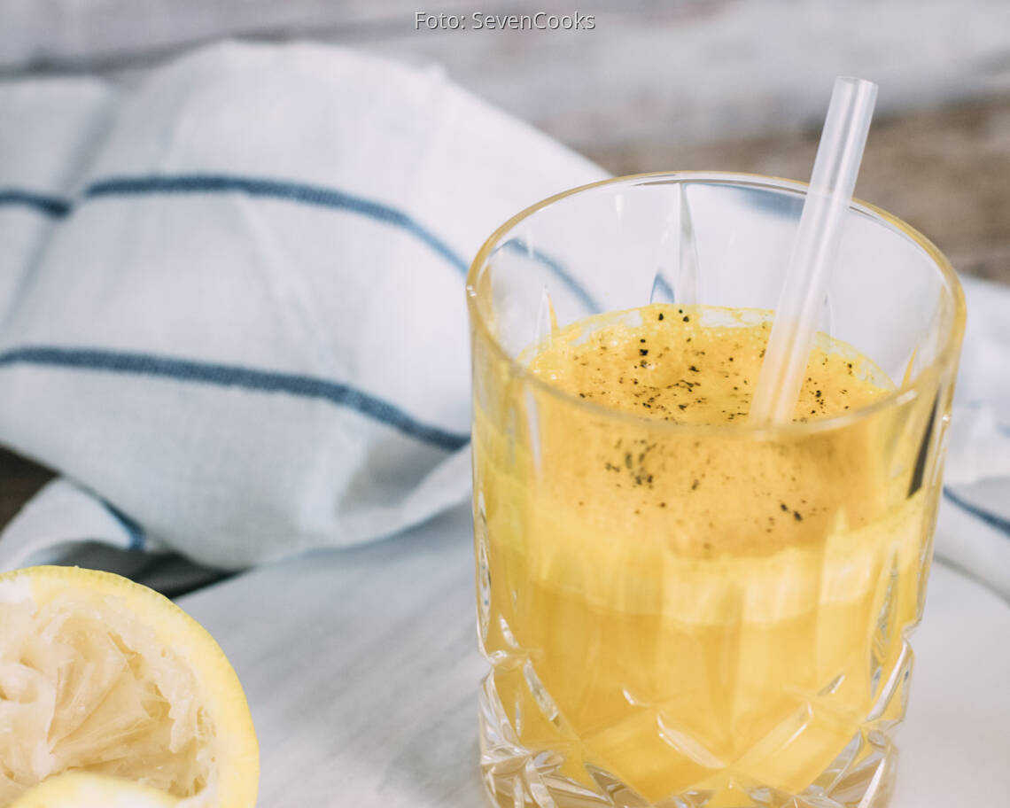 Gelber Kurkuma-Ingwer Immunbooster in Glas mit Strohhalm.