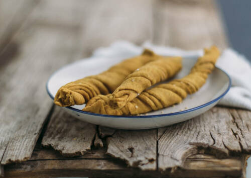 Knusprige Kurkumabrotstangen auf einem Teller, von der Seite fotografiert.