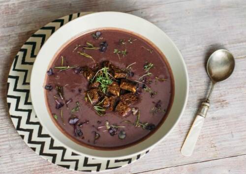 Garantiert ein Hingucker: Lila Süßkartoffelsuppe mit Rosmarin-Croutons, daneben ein Löffel. Von oben fotografiert.