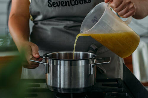 Linsen kochen in Topf mit Brühe vor dunklem Hintergrund.