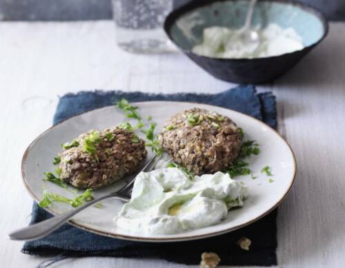 Linsen-Nuss-Laibchen mit Schmand auf weißem Teller vor hellem Hintergrund.