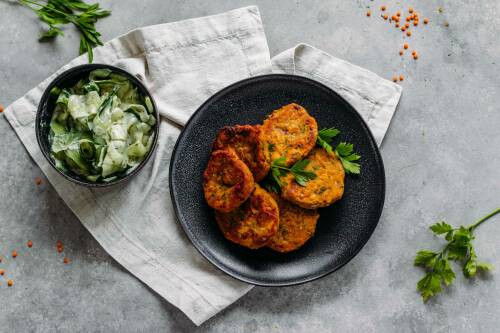 Linsenfrikadellen mit Gurkensalat in Teller und Schüssel vor hellem Hintergrund.
