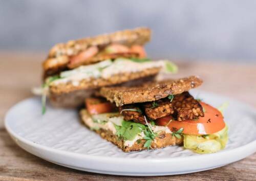 Knuspriger Tempeh in saftigem Eiweiß-Toastbrot, dazu gesellen sich Tomaten.