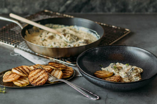 Low Carb Kohlrabi Steaks in Pfanne und Teller neben Pilzsoße vor dunklem Hintergrund.