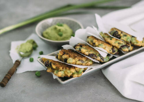 Mais-Gemüse-Puffer mit Erbsen-Hummus auf einer Platte von oben fotografiert.