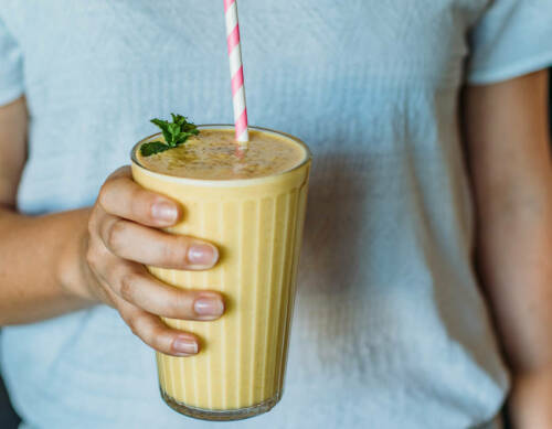 Mango-Lassi in Glas mit Strohhalm und Hand vor blauem Hintergrund.