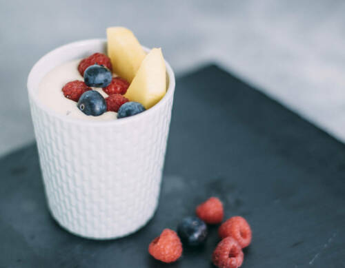 Mango-Quark-Dessert mit Früchten in Becher vor dunklem Hintergrund.