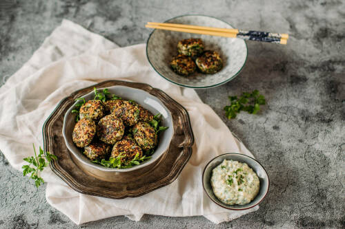 Mangold Quinoa Bratlinge auf Tellern mit Stäbchen und Soße vor dunklem Hintergrund.