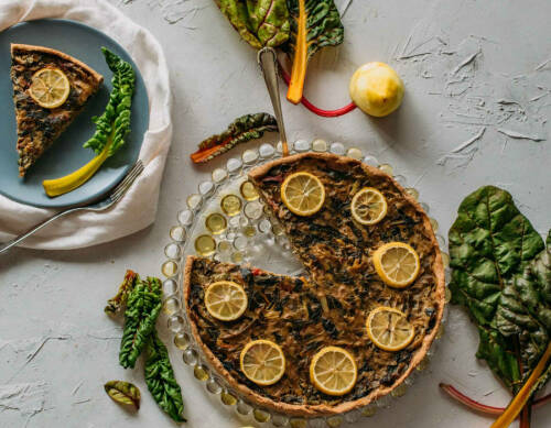 Mangold-Zitronen-Quiche neben Mangold vor hellem Hintergrund.
