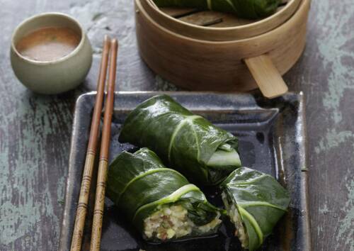 Päckchen aus Mangold-Blättern auf einer Platte, dazu Dip und Stäbchen, von