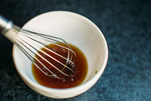 Marinade in weißer Schüssel mit Schneebesen vor dunklem Hintergrund.