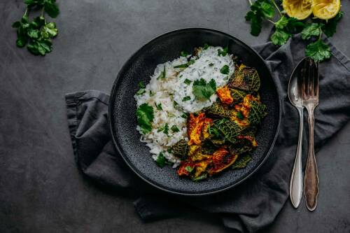 Marinierter Wirsing aus dem Ofen in schwarzem Teller neben Besteck vor dunklem Hintergrund.