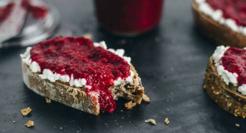 Scheibe Brot mit Hüttenkäse und Himbeer-Chia-Marmelade drauf. Von der Seite fotografiert.