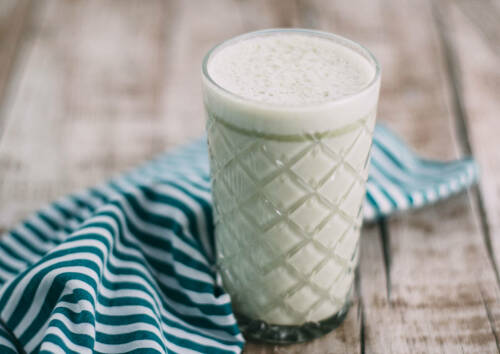 Frühstücksgetränk Matcha Latte in einem hohen Glas auf einem Holztisch,  von vorne fotografiert.