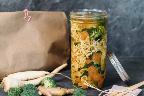 Mie-Suppe in Glas neben Suppengrün vor hellem Hintergrund.