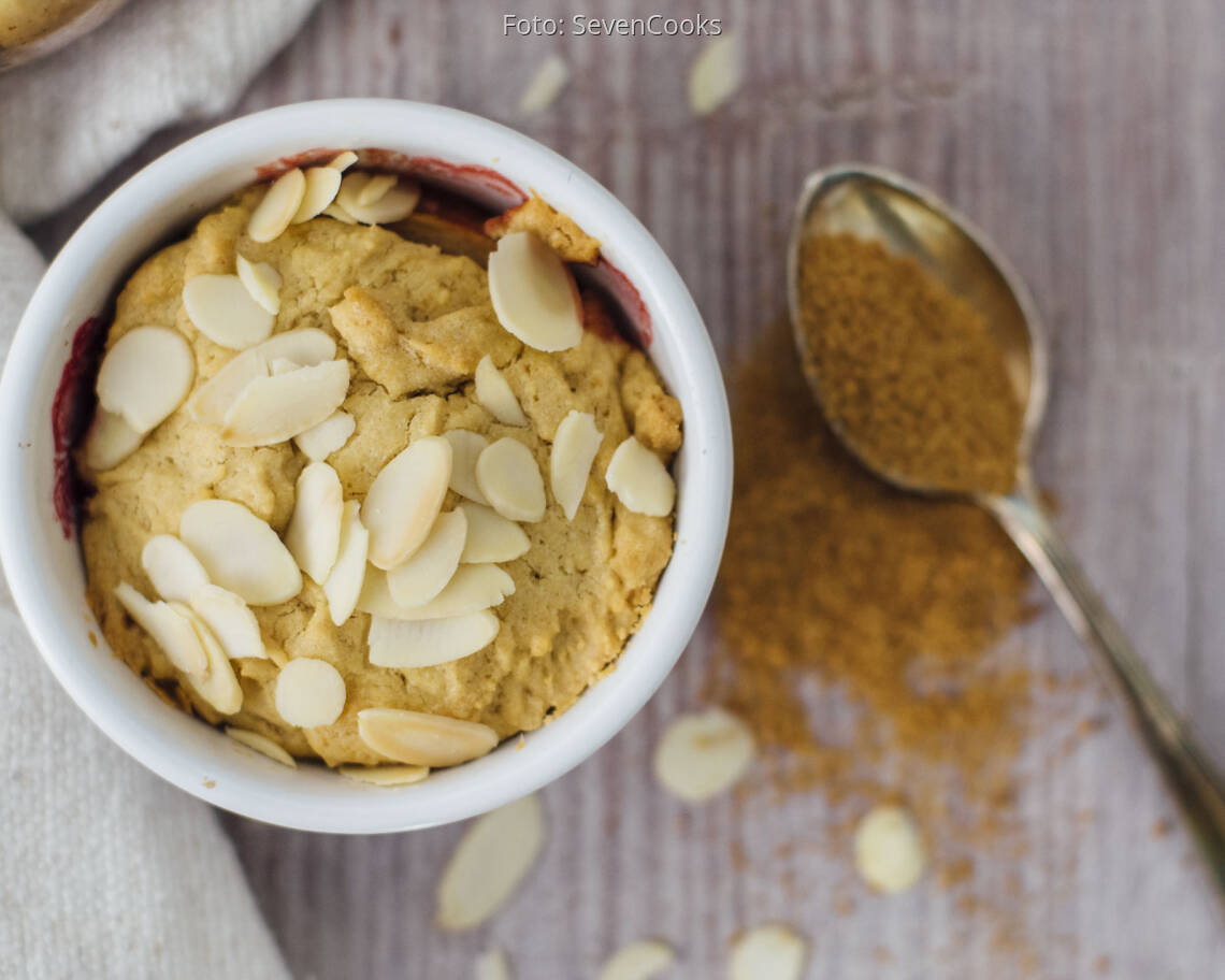 Ein kleiner Auflauf von oben mit Kokoszucker auf einem Löffel und Mandelblättchen