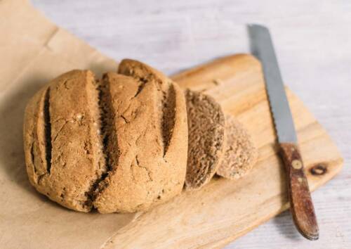 Kleiner Laib Mischbrot auf einem Holzbrett, daneben ein Messer. Das Brot ist angeschnitten und wurde von oben-seitlich fotografiert.