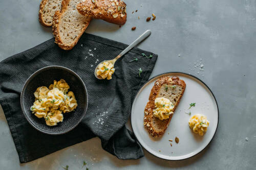 Miso-Butter auf Brot und in Schüssel neben Butter und Löffel vor dunklem Hintergrund.