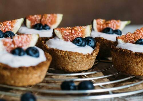 Auf einem Gitter stehen mehrere kleine Törtchen bestehend aus einer knusprigen Nuss-Kruste gefüllt mit Skyr, Blaubeeren und Feigen. Von der Seite fotografiert.