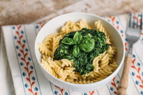 Nudeln mit Spinatsoße in Schüssel vor hellem Hintergrund.