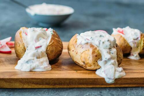 Ofenkartoffeln mit Radieschenquark auf Schneidebrett vor dunklem Hintergrund.