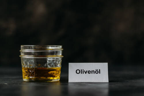 Olivenöl in Glas vor dunklem Hintergrund.