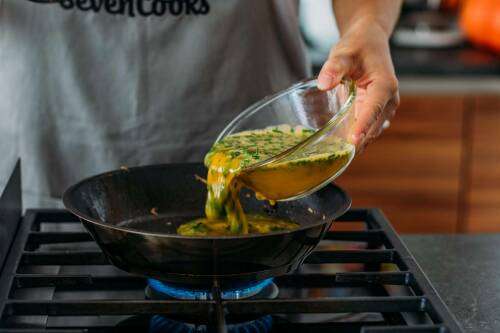 Omelett braten in Pfanne auf Gasherd vor dunklem Hintergrund.