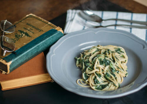 Spinat-Pasta auf grauem Teller, Besteck im Hintergrund, von oben fotografiert