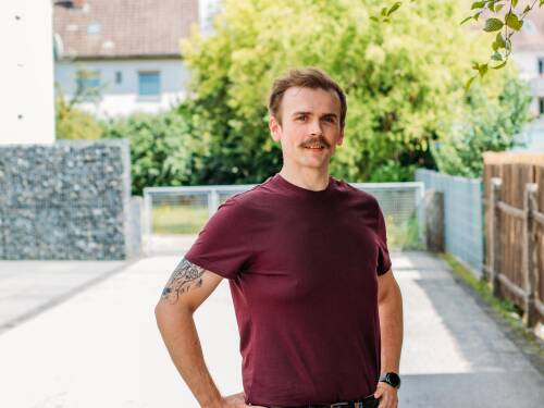 Webentwickler Paddy in einem roten T-Shirt vor einem Baum.