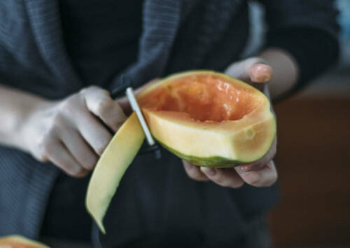 Eine halbe Papaya wird mit Sparschäler geschält.