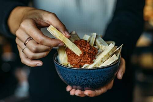 Pastinaken Pommes mit Aprikosen-Ketchup in Schüssel und Händen vor dunklem Hintergrund.