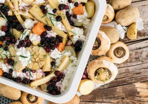 Herbstliches Ofengemüse in einer Auflaufform mit Pastinaken, Karotten, Brombeeren und Hüttenkäse. Von oben fotografiert.