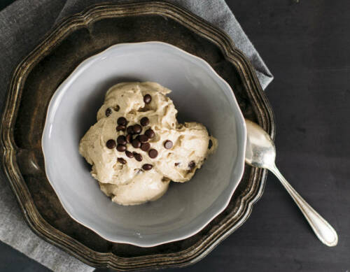 Erdnussbutter Eis in weißer Schüssel mit Löffel vor dunklem Hintergrund.