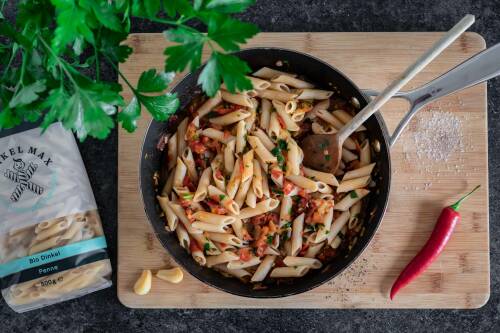 Penne all'Arrabbiata in einer Pfanne auf einem Holzbrett.