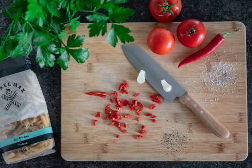 Geschnittene Chili-Schoten und halbierter Knoblauch auf einem Holzbrett.