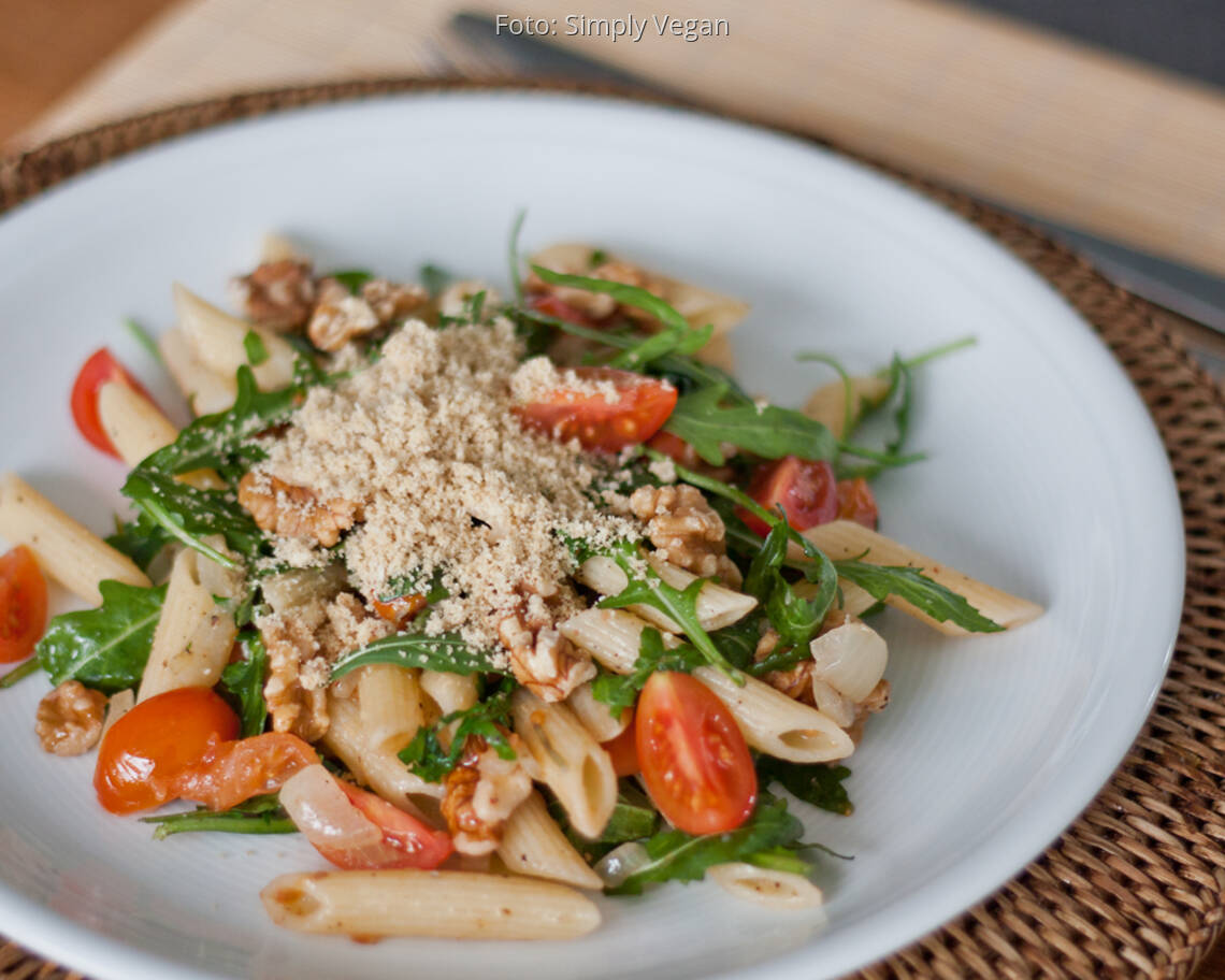 Teller mit Penne, Pucola, frischen Tomaten und veganem Parmesan