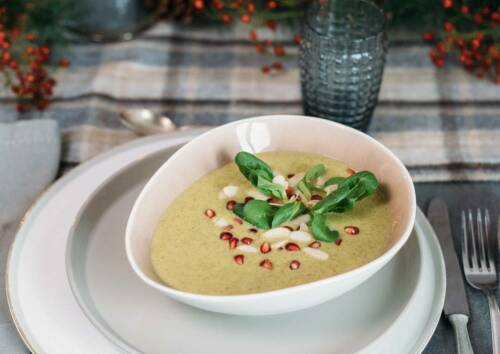 Saftig grüne Petersilienwurzelsuppe mit Feldsalat und Granatapfelkernen in einer Schüssel auf einem weihnachtlich gedeckten Tisch. Von oben fotografiert.