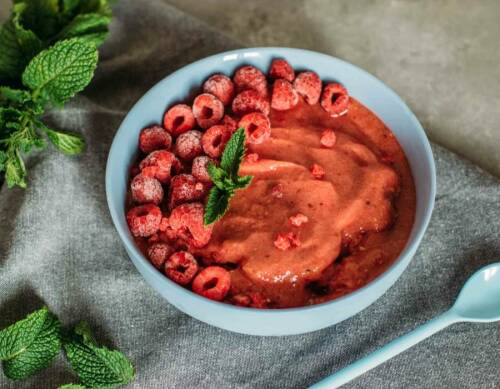 Pfirsich-Himbeer-Eis in Schüssel mit Minze vor dunklem Hintergrund.