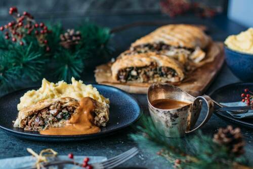 Pilzbraten mit Kartoffelstampf neben Tannenzweigen und Bratensoße vor dunklem Hintergrund.