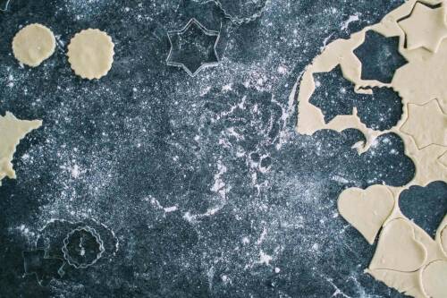 Bereits ausgestochene Plätzchen, Mehl- und Teigreste und Plätzchen-Ausstecher von oben fotografiert.