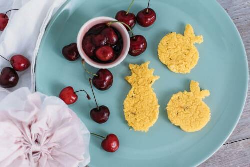 Polentaplätzchen mit Kirschgrütze auf türkisem Teller vor hellem Hintergrund.