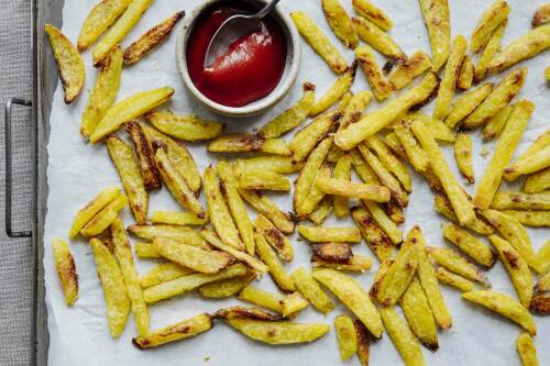 Pommes auf Backblech neben Ketchup vor hellem Hintergrund.