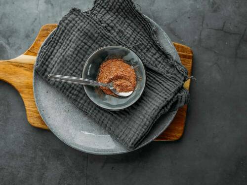 Pommesgewürz in Schüssel auf Teller und Geschirrtuch vor dunklem Hintergrund.